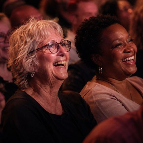 A woman laughing into her hand next to her friend