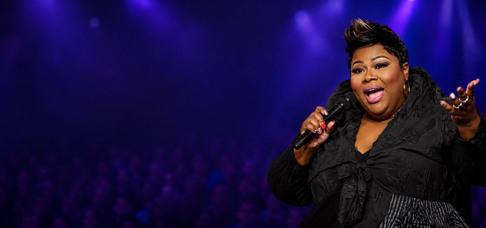 Tanya Lewis performing on stage with a microphone under purple lights